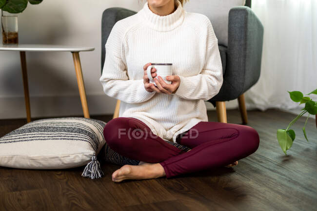 Femme tenant tasse de café jambes croisées sur le sol — Photo de stock