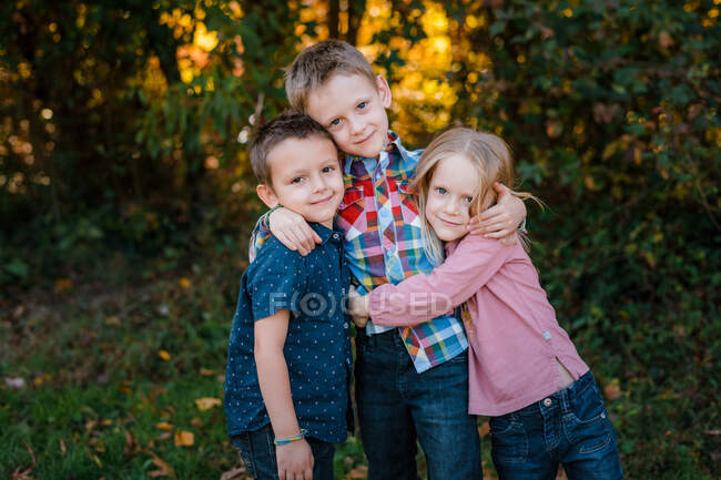 Brothers and sister embracing outdoor family portrait — Stock Photo