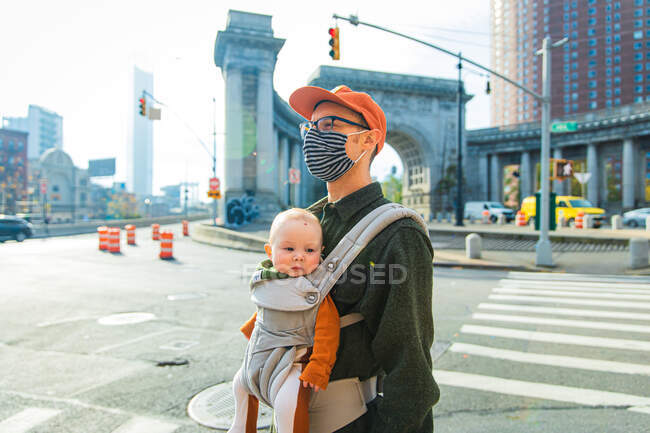 Vater trägt Tochter in Tragetasche, während er während der Coronavirus-Pandemie auf der Straße in der Stadt läuft — Stockfoto