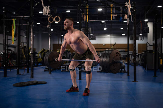 Atleta masculino sudoroso gruñendo y levantamiento de pesas pesadas barras mientras entrena en el gimnasio - foto de stock