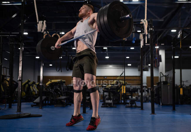 Низкий угол у сильного мужчины в спортивной одежде, поднимающего штангу на цыпочках во время упражнений 
