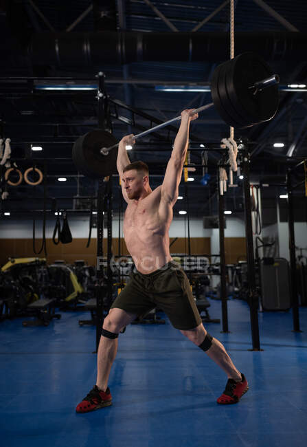 Deportista enfocado dando un paso adelante mientras hace ejercicio limpio y tirón en el gimnasio - foto de stock
