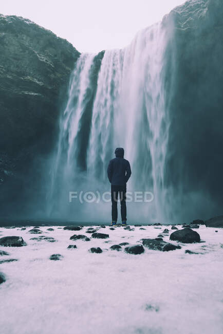 Person standing at Skogafoss waterfall in the winter with snow in foreground — Stock Photo