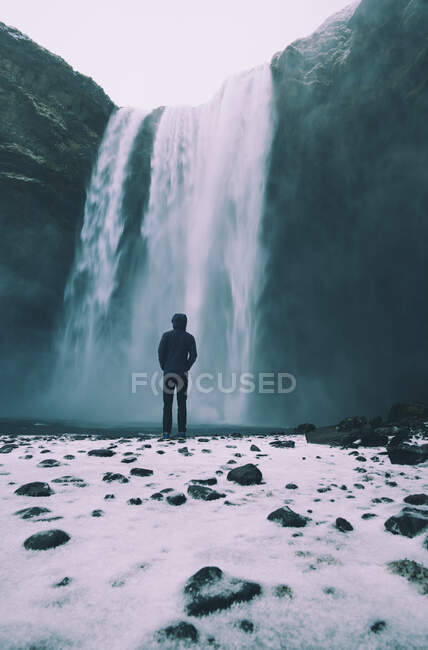 Person standing at Skogafoss waterfall in the winter with snow in foreground — Stock Photo