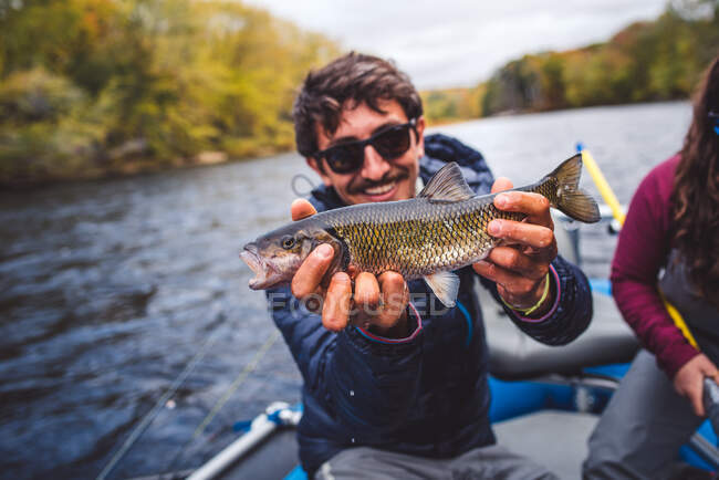 Man holds chub fish out in front of him in a boat — Stock Photo