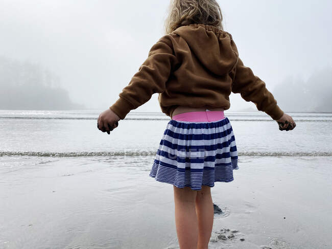 A young girl plays in the sand on the coast of OR on a foggy day. — Stock Photo