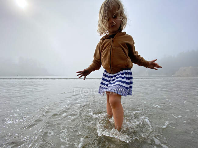 Una giovane ragazza gioca nell'oceano in una giornata nebbiosa sulla costa della sala operatoria. — Foto stock