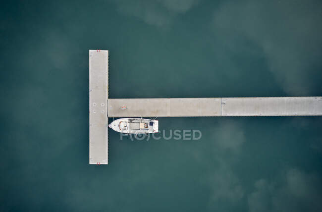 Aerial top view of lonely motorboat moored at long T shaped jetty in blue ocean water — Stock Photo