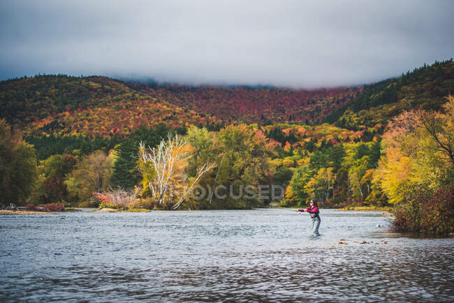 Woman angler casting into river with clouds and bright foliage — Stock Photo