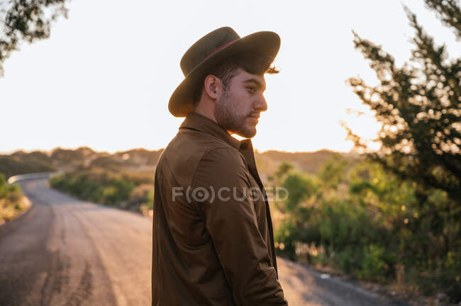 Hombre explorador guapo de pie en el camino y disfrutando del amanecer - foto de stock