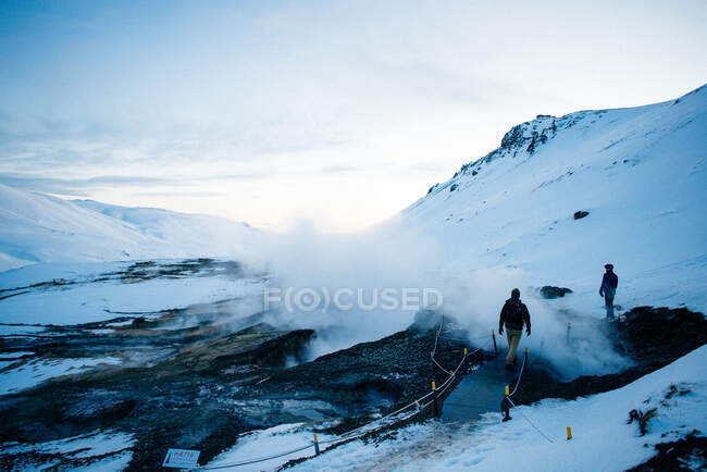 Двоє людей проходять повз геотермальні басейни до річки Рейк'ядалур — стокове фото