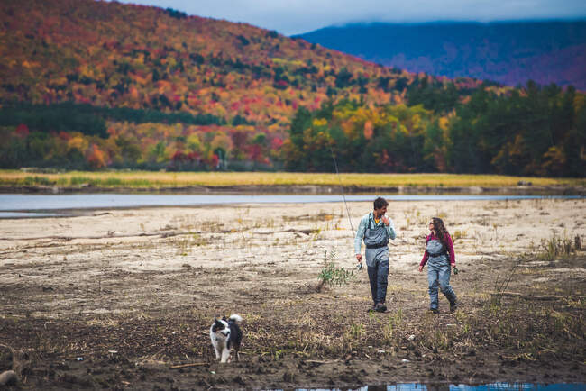 Male and female anglers walk down the shore with dog and foliage — Stock Photo