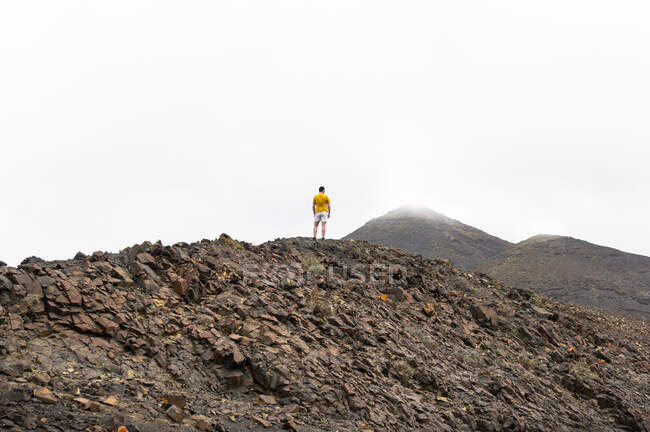 Rückansicht eines Mannes, der zwischen Wolken auf einem hohen Berg steht. — Stockfoto