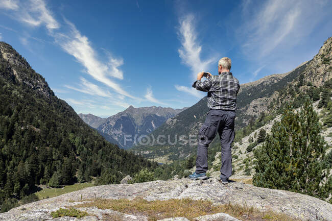 Homem de meia-idade turista tirar fotos com telefone celular em espanhol Pirinéus montanha em um dia ensolarado — Fotografia de Stock