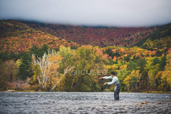 Vola pescatore gettando nel fiume con nuvole e fogliame luminoso — Foto stock