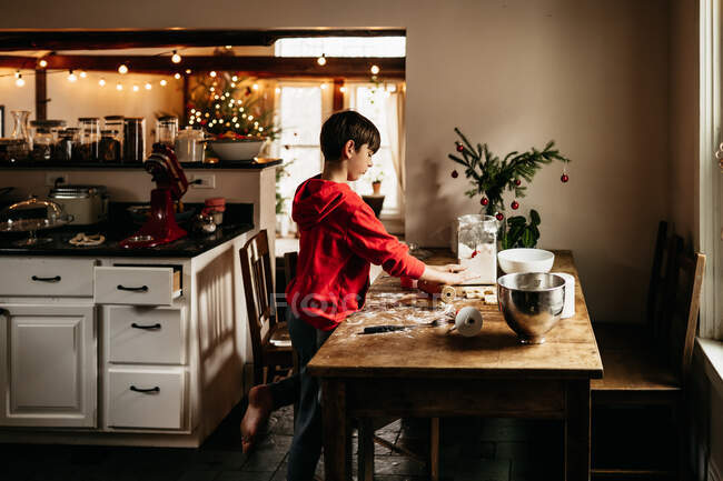 Child making cookies in his kitchen, with Christmas tree in background — Stock Photo