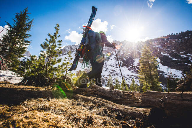 Low angle of man walking in mountains with skis on backpack — Stock Photo