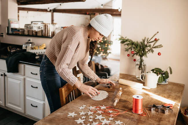 Giovane donna che crea ornamenti stellari con argilla per Natale in cucina — Foto stock
