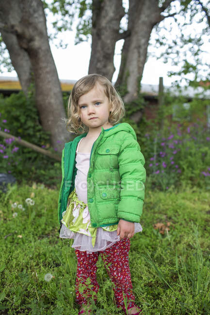 A portrait of a young girl wearing a green jacket in the backyard. — Stock Photo