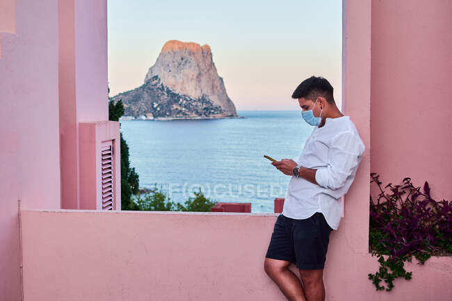 Junger Mann hält sein Handy in einem rosafarbenen Gebäude — Stockfoto