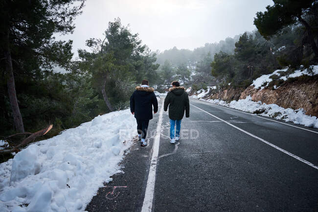 Dos amigos caminan por un camino rodeado de nieve - foto de stock