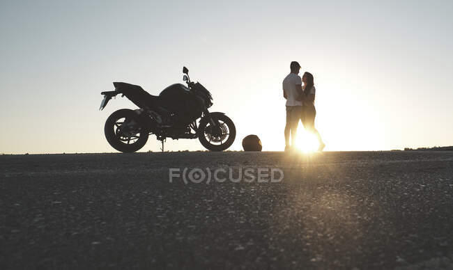Retroilluminazione di una coppia in posa sulla strada con la loro moto — Foto stock