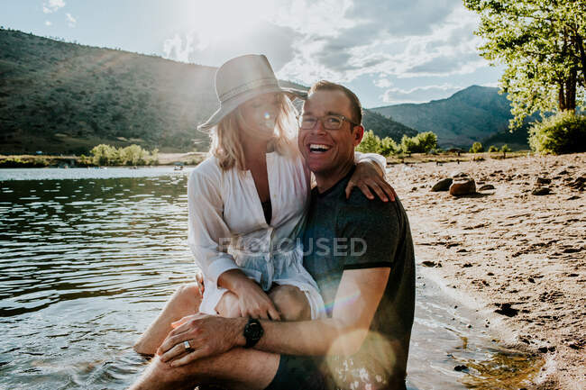 Portrait of a young couple hugging and laughing on lakeshore — Stock Photo