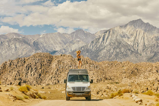 Young woman on roof of camper van on road in northern California — Stock Photo