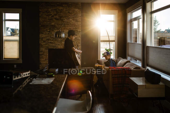 Брати грають вдома на гітарі, сонце заходить у вікно. — стокове фото