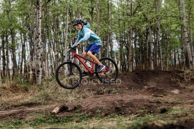 Мальчик-подросток на горном велосипеде в парке грязи делает прыжки — стоковое фото