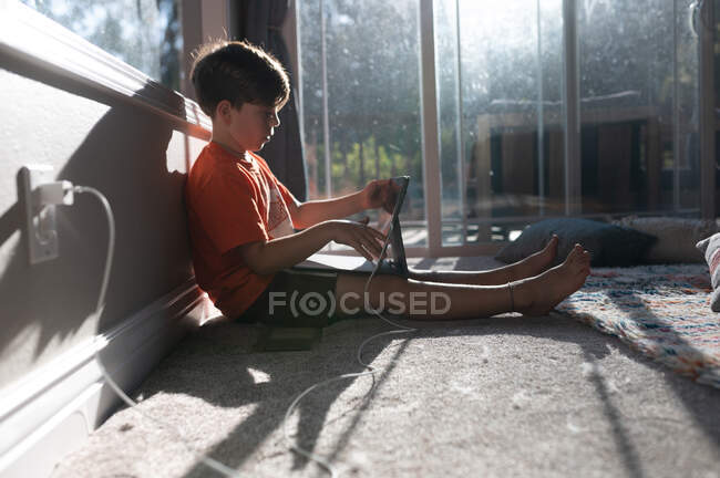 Profile of boy using ipad tablet on the floor of his home — Stock Photo