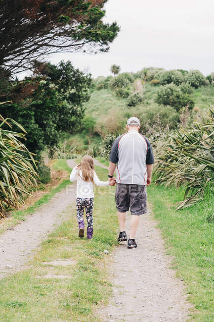 Padre e figlia che camminano lungo un sentiero panoramico tenendosi per mano — Foto stock