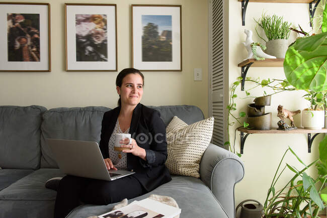 Mujer joven con ordenador portátil sentado en el sofá - foto de stock