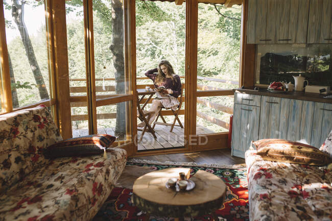 Молода жінка читає газети на балконі дерев'яного будинку — стокове фото
