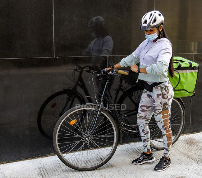 Дівчина з її велосипедом і зеленою коробкою перед чорною стіною і дивиться — стокове фото