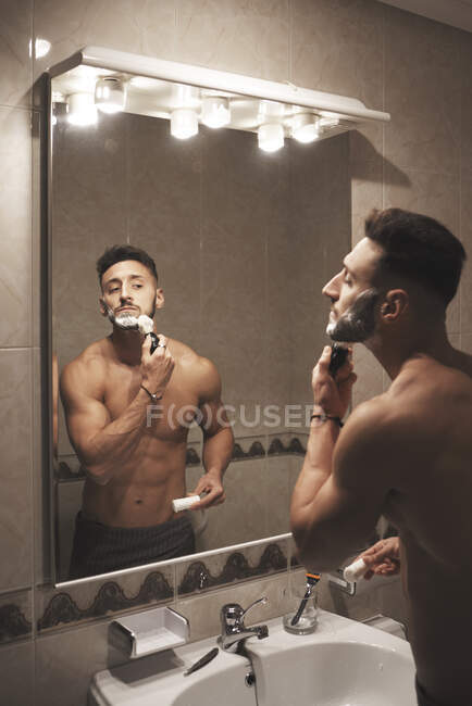 Un ragazzo è davanti allo specchio di fronte al viso con schiuma — Foto stock