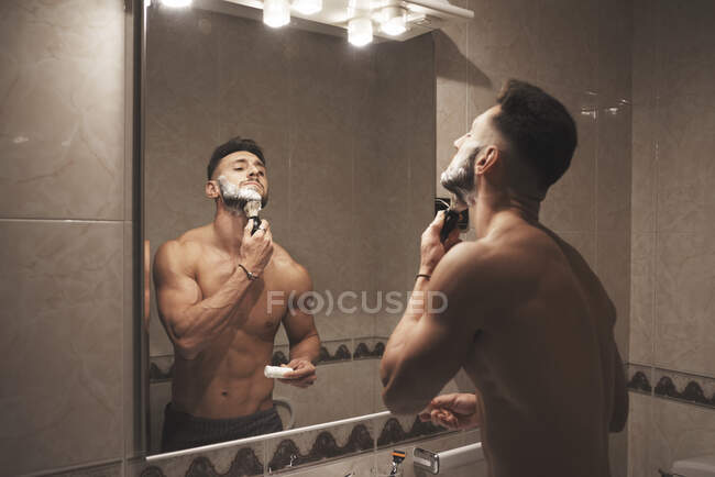 Um menino forte e bonito esfrega seu rosto com uma escova cheia de espuma — Fotografia de Stock