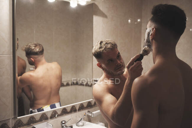 Um rapaz esfrega a cara de outro rapaz com uma escova de barbear. — Fotografia de Stock