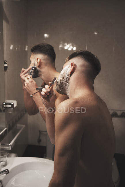 Vista lateral de dos hombres afeitándose juntos en el baño - foto de stock