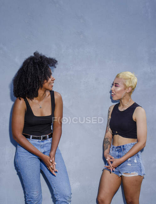 Dos mujeres jóvenes riendo en ropa idéntica se paran riendo juntas - foto de stock