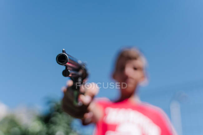 Blonde teenager wearing a red t - shirt pointing with a gun. — Stock Photo