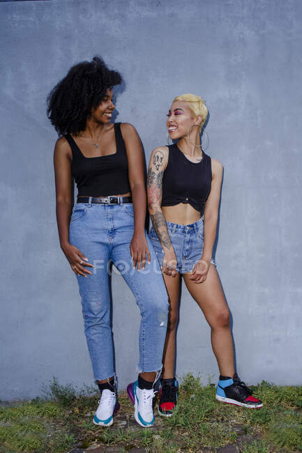 Dos amigos sonrientes se apoyan juntos contra una pared en ropa a juego - foto de stock