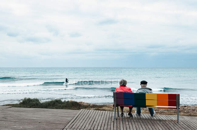 Un vieux couple assis sur un banc coloré regardant vers la mer — Photo de stock