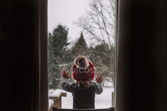 Menina olha pela janela durante um dia de neve no inverno — Fotografia de Stock