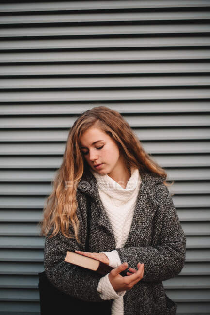 Портрет девочки-подростка с книгой, стоящей у серой стены — стоковое фото