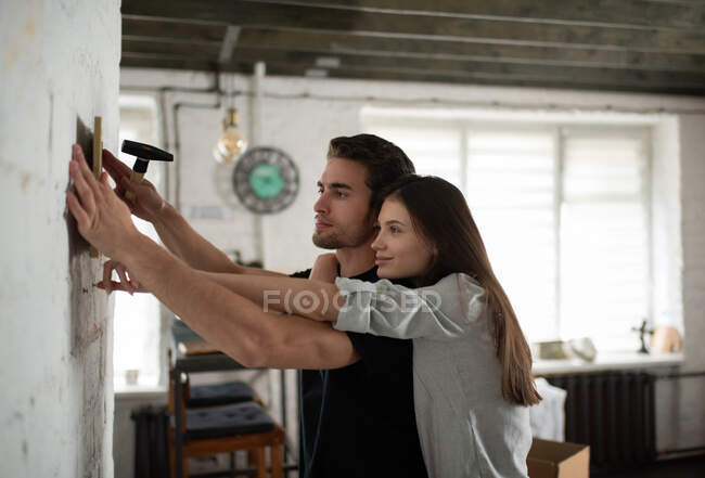 Seitenansicht der jungen Frau umarmt Freund, während Hängerahmen mit Bild an der Wand während des Umzugs in neue Wohnung — Stockfoto
