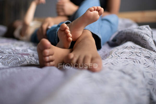 Unrecognizable barefoot woman and kid lying on soft bed and playing while spending time at home together — Stock Photo