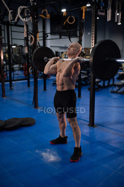 Athlète masculin âgé de corps entier en grande forme soulevant l'haltère lourde tout en faisant l'exercice propre et secousse pendant l'entraînement fonctionnel dans la salle de gym — Photo de stock