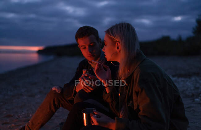 Вид сбоку молодой пары, курящей марихуану, сидя на природе в пасмурную осеннюю ночь — стоковое фото