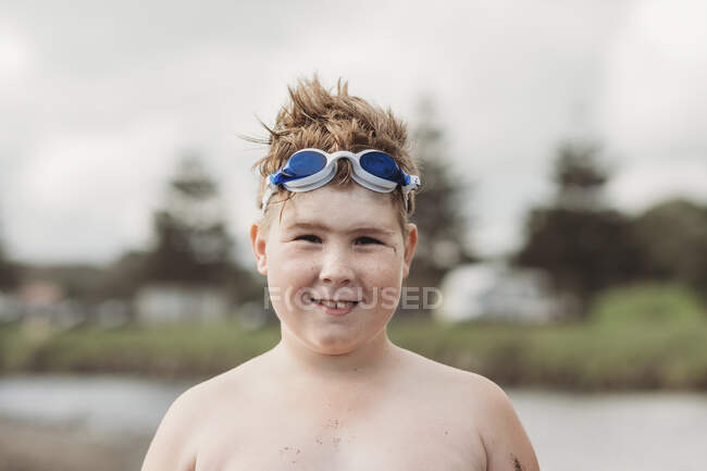 Chico sonriente en la playa con gafas en la parte superior de su cabeza - foto de stock